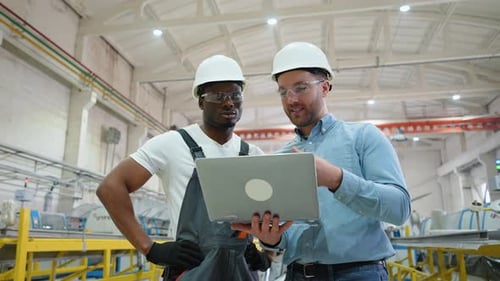 Two Factory Workers Working and Discussing Manufacturing Plan in the Factory