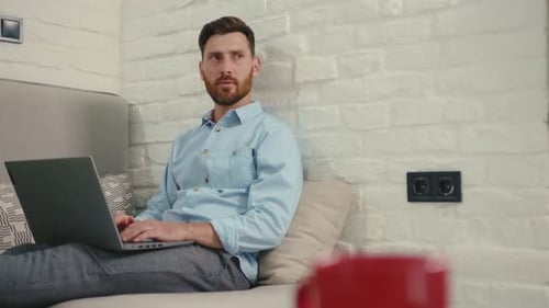 Man Working on Laptop While Relaxing on Couch