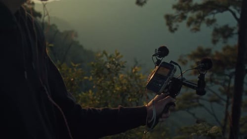 A Young Man is Holding a Microphone Amidst a Serene Forest Setting Surrounded By Nature