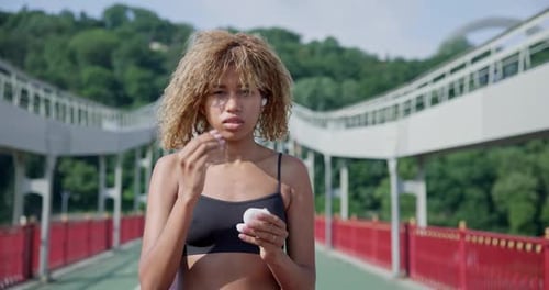 Young African American Woman Putting on Earphones Before Jogging Outdoors on City Bridge