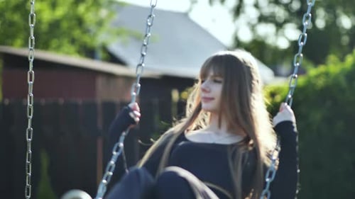 Une fille aux cheveux blonds vêtue d'une robe noire monte sur une balançoire