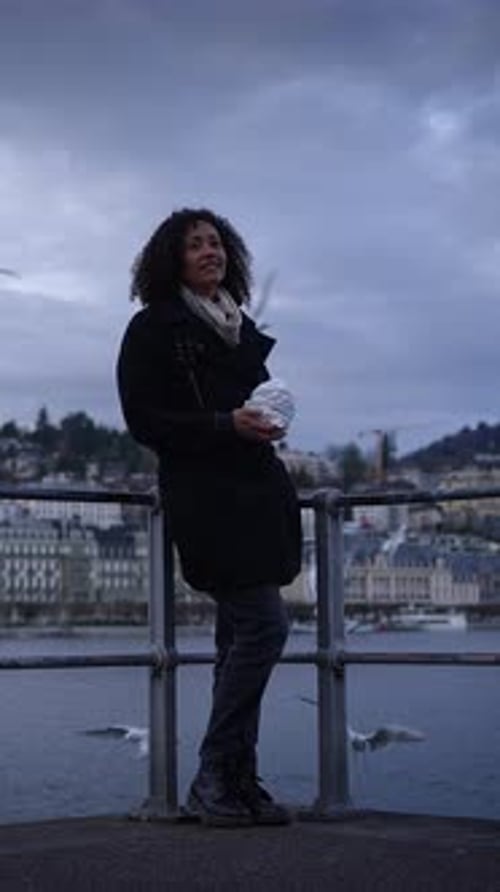 Woman feeding seagulls on waterside platform