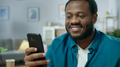 Smiling Man Using Smartphone Device in Home Living Room