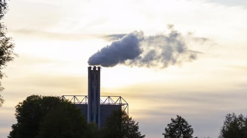 Time lapse of smoking factory chimney against the background of a setting sun