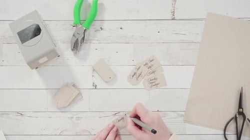 Hands Writing Christmas Tags with Paper and Pen