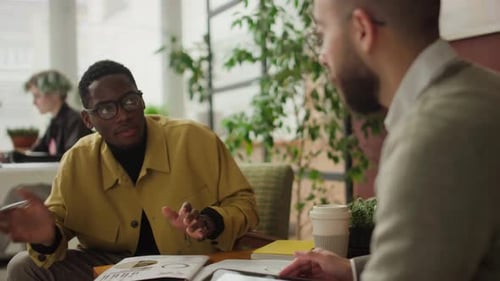 Afroamerikanischer Mann und kaukasischer Kollege sprechen am Kaffeetisch