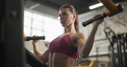A Young Beautiful Brunette Girl in Sportswear is Exercising on a Machine in the Gym Doing Exercises
