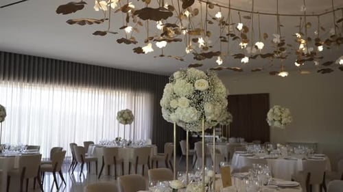 Elegant reception hall with white floral centerpieces and golden ceiling decor.