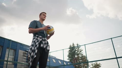 Young Man Rotating Volleyball in Hand with Plaid Shirt and Outdoor Court Background