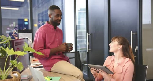 Smiling diverse colleagues in modern office, man holding coffee and woman using tablet