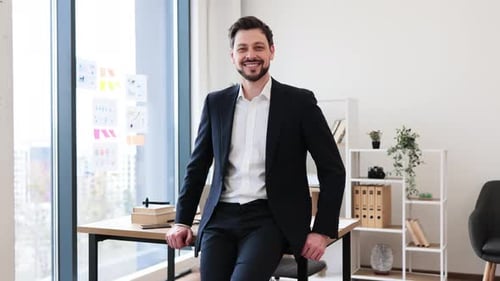 Confident Businessman Sitting on Desk in Modern Bright Office Workspace