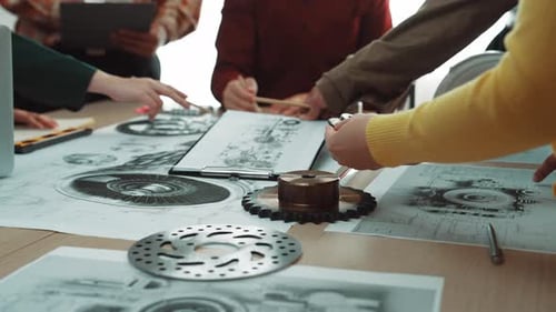 Collaborative Workshop Setting with Diverse Hands Working on Mechanical Engineering Plans and Diagra