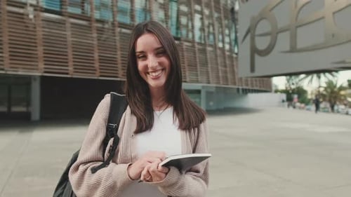 Girl student with notebooks in her hands stands outside the university looks at the camera