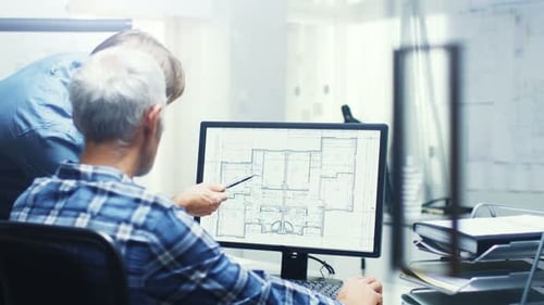 Two Senior Architectural Engineers Working With Building Plan on a Personal Computer. They Actively