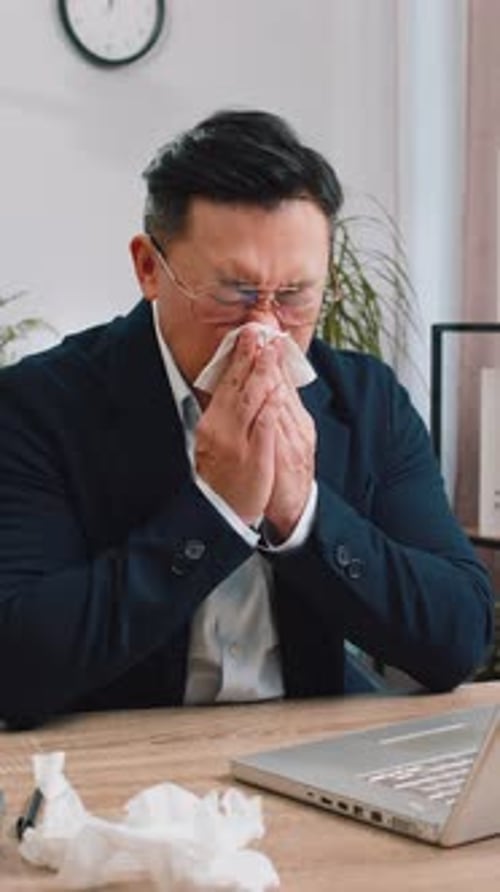 Businessman Suffers From Cold Flu Fever or Allergy Sneezes Wipes Snot Working on Laptop at Office