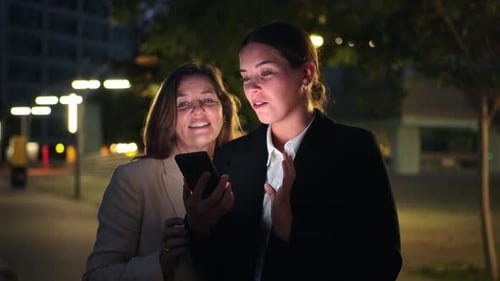 Two Women Using Smartphone at Night in City