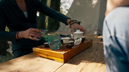 The hands of a professional tea master who pours fresh natural green tea from a glass teapot