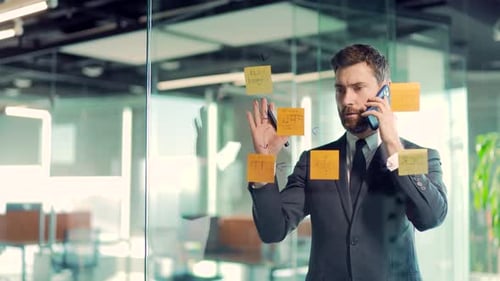 business man talking on the phone in a modern office behind a glass task partition wall with paper