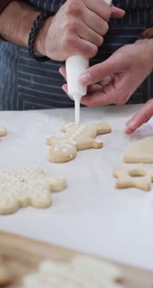 Vertical video of midsection of caucasian man decorating christmas cookies, slow motion