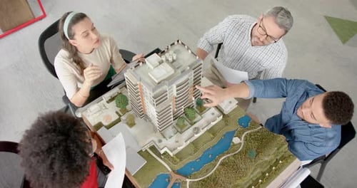 Blick von oben auf ein Team verschiedener Ingenieure, die im Büro über ein 3D-Gebäudemodell diskutieren