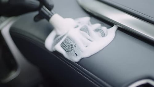 Closeup of a Hand in a Black Glove Washing the Dashboard of a Car Interior with a White Brush with