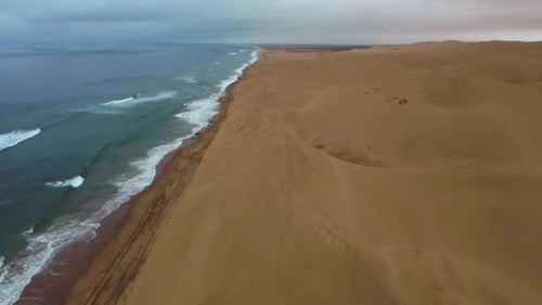 Descending drone shot of Sandwich Harbour in Namibia - drone is following the coastline where desert