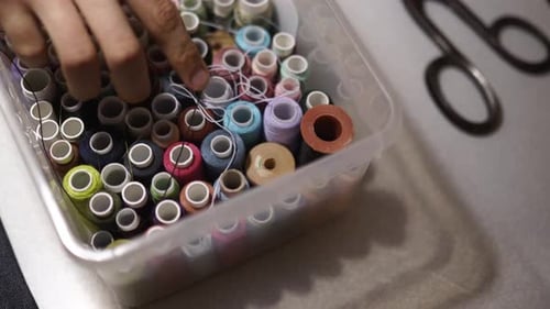 Hand Selecting Colorful Spools of Thread in Container