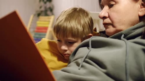 Woman Reads Book with Young Boy at Home