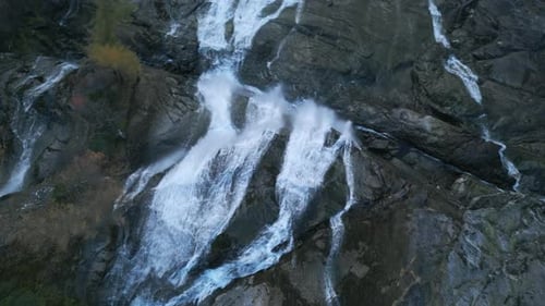A waterfall cascading down rocky cliffs surrounded by nature and greenery, aerial view
