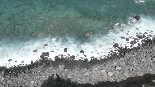 volcanic rocks on beach, black rocks beside water, waves crashing on rocks