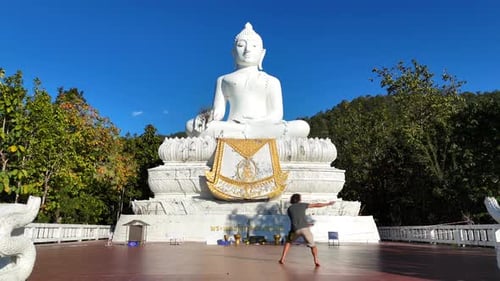 Man Balances Before Large White Buddha Statue