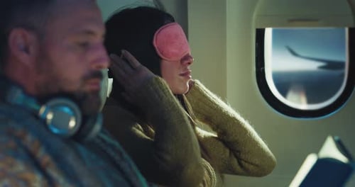 Cinematic shot of young woman puts on sleep mask for napping while her husband reading book in air