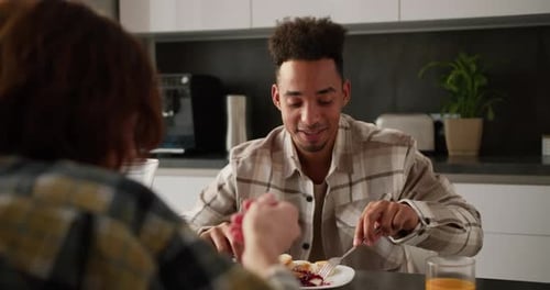 Over the Shoulder a Happy Young Blackskinned Brunette Man in a Cream Plaid Shirt Eats Cheesecakes