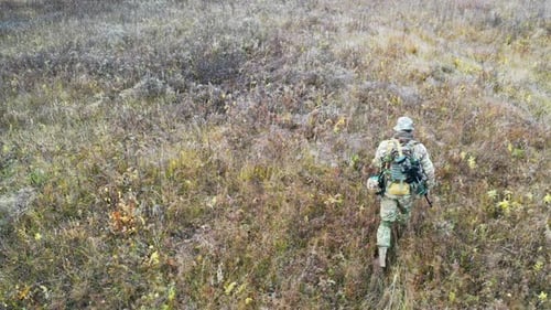 Adult in Camouflage Walks in Grassy Field