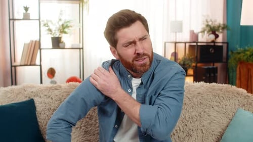 Man Rubbing Sore Shoulder On Couch