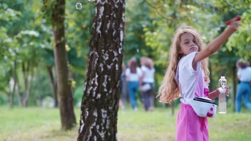 Little girl blowing soap bubbles. Little cute blonde girl blowing bubbles in park