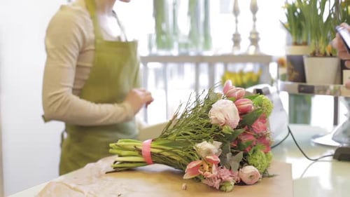 Florist woman counts bunch cost at cashbox as man pays with credit card at flower shop