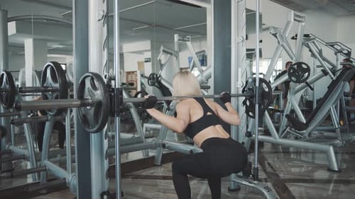 Woman trains in gym with barbell while focusing on strength and form