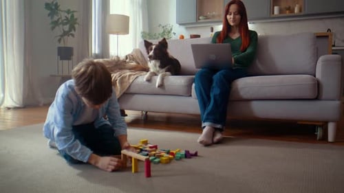 Un niño construye bloques de colores mientras una mujer trabaja en una computadora portátil en casa