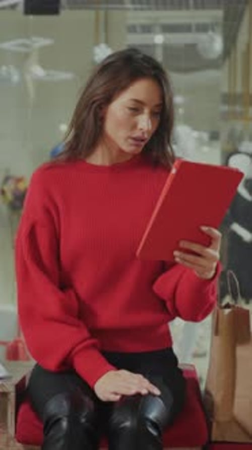 Woman Dressed in Cozy Winter Clothing Engaging with Holiday Promotions on Her Device in Shopping