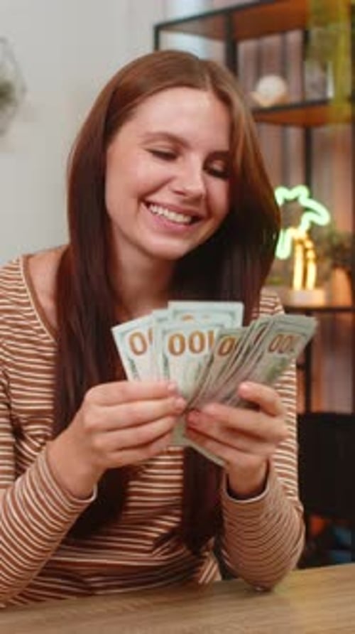 Woman Counts Cash Dollar Bills Money at Table Smiles Pleased About Salary Lottery Win Savings Income
