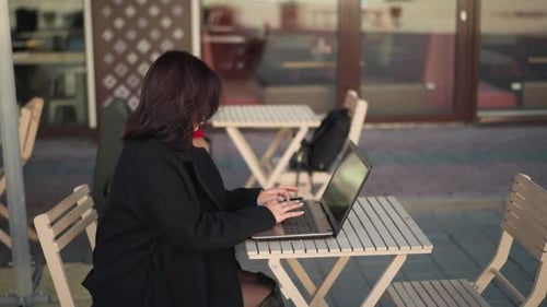 Side View of Woman Typing on Laptop in Urban Restaurant Setting