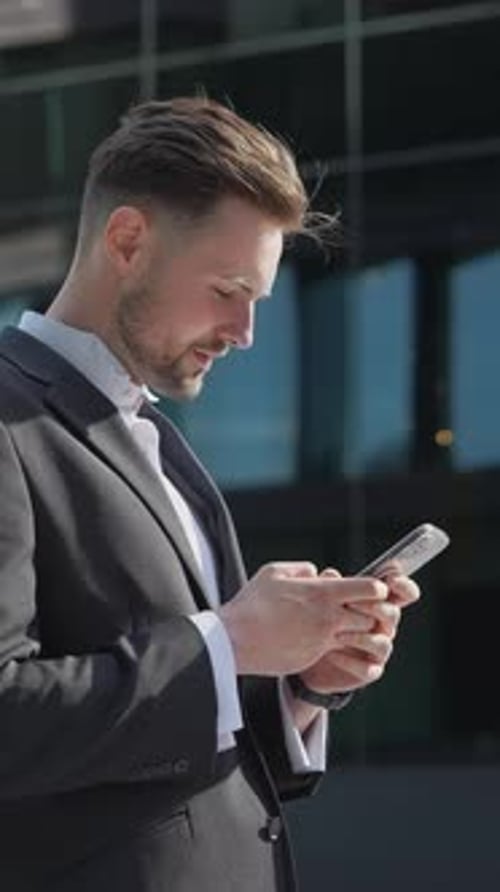 Young Businessman Holding Phone Reading Email Stands on Street Smiling Writes Message Communicates