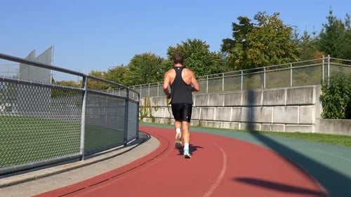Sportsman Running On A Sports Track During Sunny Day. Tracking Shot