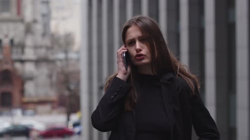A Longhaired Brunette Woman Stands in the Middle of the Street and Discusses Something on the Phone