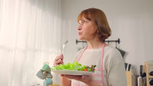 Caucasian senior woman eating a bowl of vegetables on hands in house.