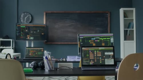 Tech Workspace with Multiple Laptops Running Software in Front of Blackboard