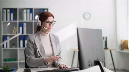 Call Center Employee Charming Woman in Glasses Talking to a Client Using a Headset While Sitting at