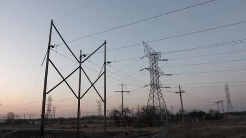 Transmission towers and electrical lines silhouetted with setting sun in background