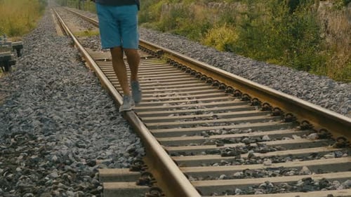 Detail der Füße eines Mannes, der auf Bahngleisen an einem möglicherweise verlassenen Bahnhof balanciert, wie er es tat, als er